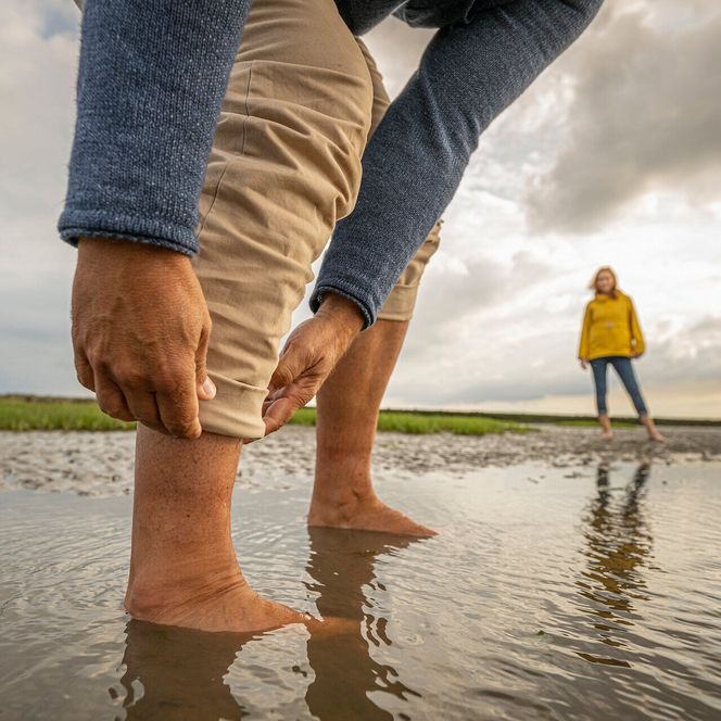 Ein Mann krempelt sich die Hose im Watt hoch
