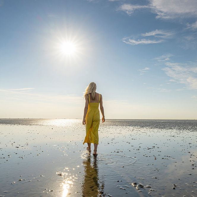 Eine Frau läuft bei Sonne durch das Watt in Cuxhaven